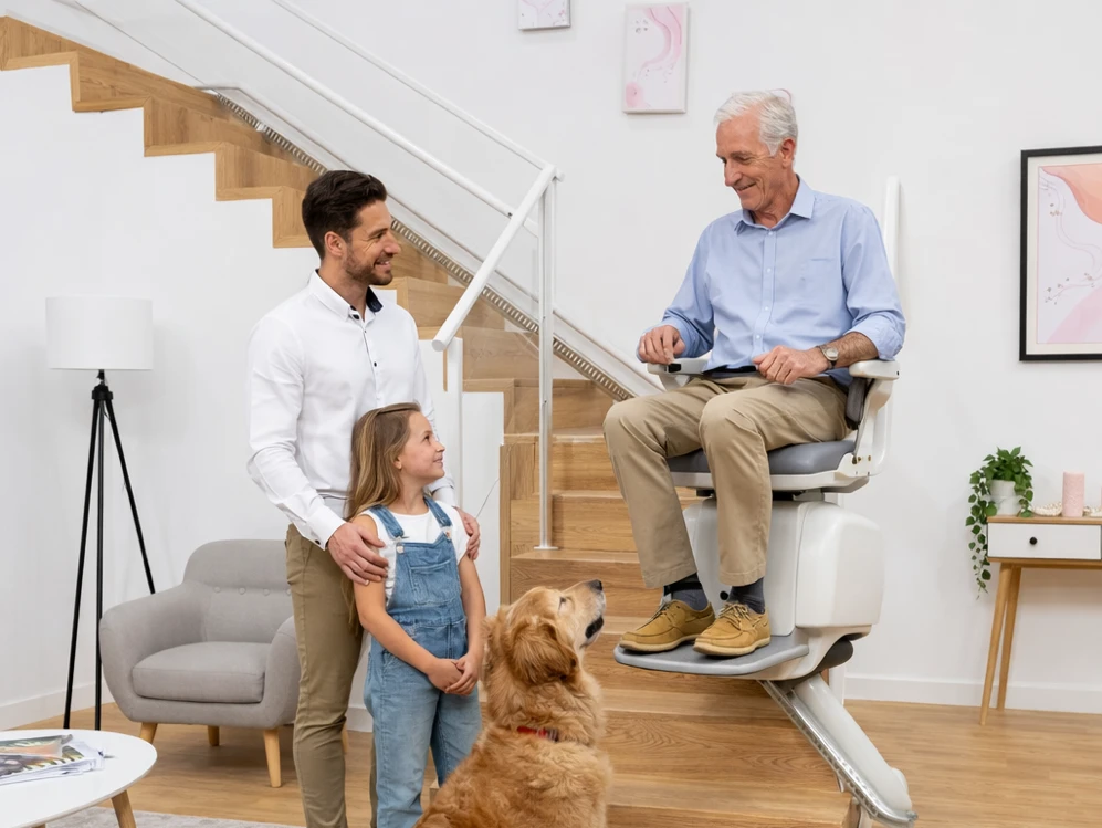 Persona mayor sentada en su silla salvaescaleras, con su familia y su perro alrededor en el salón de casa