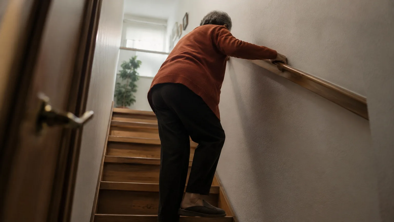 Persona mayor subiendo la escalera de su casa agarrada al pasamanos con las dos manos