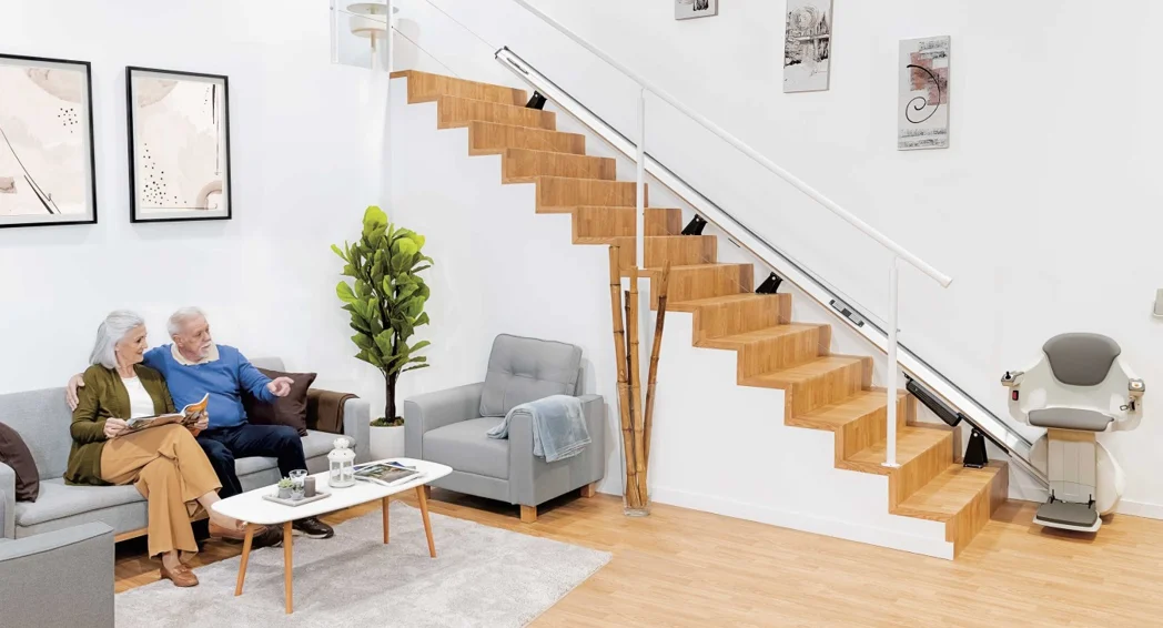Pareja mayor en el salón de su casa junto a una silla salvaescaleras